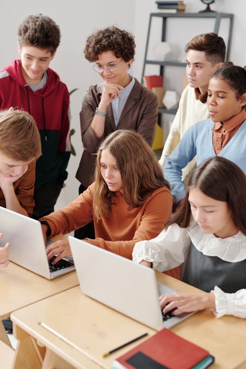 image of 5 kids watching 2 kids do school work on a computer